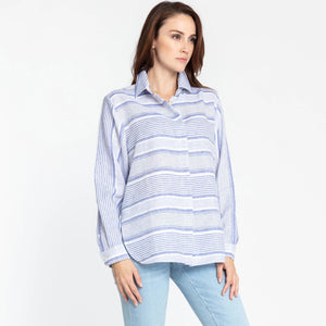 A person with long brown hair is wearing the HINSON WU - GEMMA LONG SLEEVE LINEN SHIRT, which features a light pink and white striped pattern and functional side button details. They have paired it with light blue jeans and are posing against a plain white background, looking directly at the camera with a neutral expression.