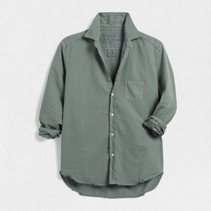 The FRANK & EILEEN - EILEEN RELAXED BUTTON UP SHIRT IN FAMOUS DENIM THYME is a light green, long-sleeved button-up shirt with a single chest pocket. The sleeves are rolled up to the elbows, and the fabric has a slightly crinkled texture. Featuring Eileen's relaxed fit, this shirt includes bust-flattering button placement, a high-low hem, and a collar without a visible tag.