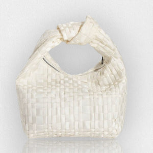 The MINI KNOT HANDLE BAG by MARIA LA ROSA is a compact and chic accessory crafted from light blue ribbon fabric. It features a distinctive knotted handle at the top and is photographed on a reflective surface, enhancing its slight sheen. Handmade in Italy, this unique bag stands out against a plain, light gray background.