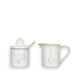 Beside a matching creamer jug, you'll find the STONEWARE SUGAR POT WITH SPOON by CREATIVE COOP. Both pieces, part of an elegant stoneware collection, feature white ceramic with embossed pine tree designs and include a subtle rustic finish that adds charm to their appearance.