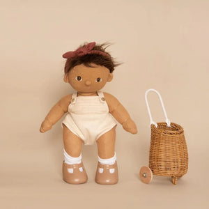 A DINKUM DOLL from OLLI ELLA USA features soft brown hair and comes dressed in a white knit romper paired with brown shoes. This charming doll has an embroidered face with brown eyes, a small nose, and a gentle smile. Its posable body makes it perfect for imaginative playtime, and it is posed standing upright.