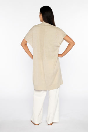 Against a white backdrop, a person with long dark hair confidently models the KINROSS Long Short Sleeve Linen Cardigan over a matching top and white wide-leg pants. One hand rests on their hip, showcasing this timeless essential from KINROSS.