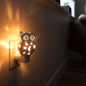 The OWL NIGHTLIGHT by LILY'S LIGHTS features a white ceramic owl design with cut-out star and moon patterns that allow light to shine through beautifully. Plugged into a white electrical base and set against a plain white background, this nightlight exemplifies quality craftsmanship, making it one of the most unique gifts.