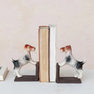 The CAST IRON JACK RUSSELL TERRIER BOOKENDS by CREATIVE COOP feature charming dog figurines with their front paws raised on a sturdy base, perfectly supporting a selection of standing books. These white dogs with distinctive brown and black markings make an ideal addition to any dog-loving bibliophile’s decor. The bookends are displayed on a light-colored surface against a neutral background.