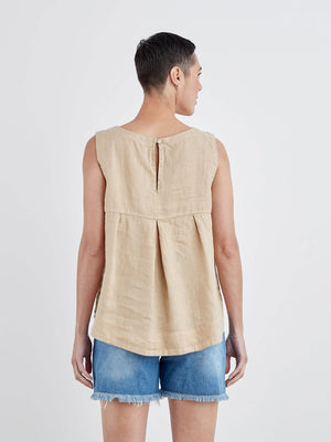 The CUT LOOSE - HI LOW TANK, a sleeveless white linen blouse with a round neckline, is displayed on a white hanger against a light gray wall. Perfect for summer wear, this breathable top by CUT LOOSE features a loose fit and an elegant high-low hem that is shorter in the front and longer in the back.