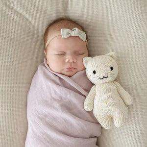 The CUDDLE + KIND - HANDMADE BABY KITTEN by CUDDLE & KIND is a knitted stuffed toy resembling a cat. It features small ears, black button eyes, and a stitched smile. Made from 100% cotton yarn, the light beige kitten has multicolored specks throughout the fabric for a textured appearance. Each purchase of this hand-knit baby animal supports fair trade income.