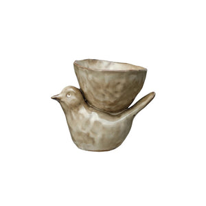 Introducing the STONEWARE BIRD WITH BOWL by CREATIVE COOP: a charming set of two ceramic measuring cups artfully designed to resemble a bird. The larger, lower cup forms the bird's body, while the smaller, upper cup perches on top, representing the bird's head and wings. Crafted from cream stoneware and featuring a rustic beige finish, this delightful piece brings avian elegance and pastoral charm to your kitchen.