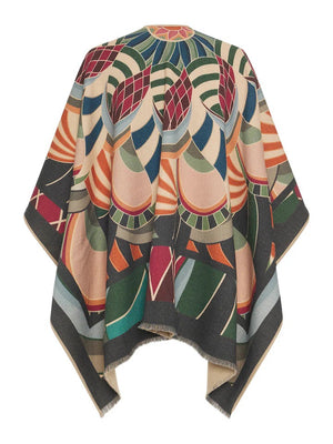 The FRANCO FERRARI PSYCHEDELIC PRINT WOOL PONCHO is displayed against a white background. This vibrant poncho features an abstract, psychedelic print with various geometric shapes and shades of green, orange, red, blue, and beige. Made in Italy by FRANCO FERRARI, it boasts an open front and a fringed hem.