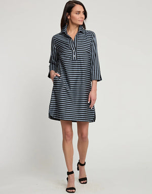 A woman stands posing sideways in a knee-length, loose-fitting HINSON WU AILEEN 3/4 Sleeve Dress featuring a classic black and tan stripe and gingham combo. She has shoulder-length dark hair and wears black high-heeled sandals. The background is a plain white wall.