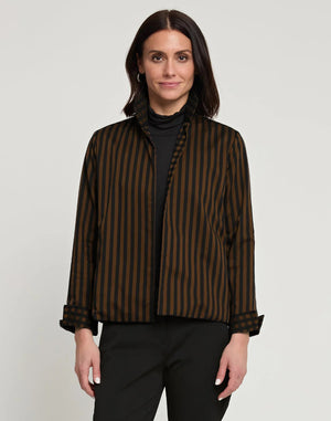 A woman with long dark hair stands against a plain background, wearing a black turtleneck, black pants, and the HINSON WU - MOLLY LONG SLEEVE REVERSIBLE JACKET made of 100% cotton. The jacket's collar and cuffs are turned up. She has one hand in her pocket and is looking off to the side with a slight smile.