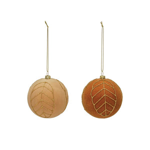 Nestled in a wooden box with straw-like filling on a light-colored surface are two VELVET BALL ORNAMENT 3" by CREATIVE COOP, one in white and the other in copper, both adorned with glittering gold leaf patterns. These ornaments add an elegant touch to any holiday decor.