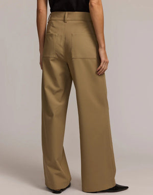 A person wears the HINSON WU - KELLY TRAVELER'S TWILL PANT—wide-leg khaki trousers with two front pockets and double button closure. Hands are in the pockets, and shoes are partially visible.