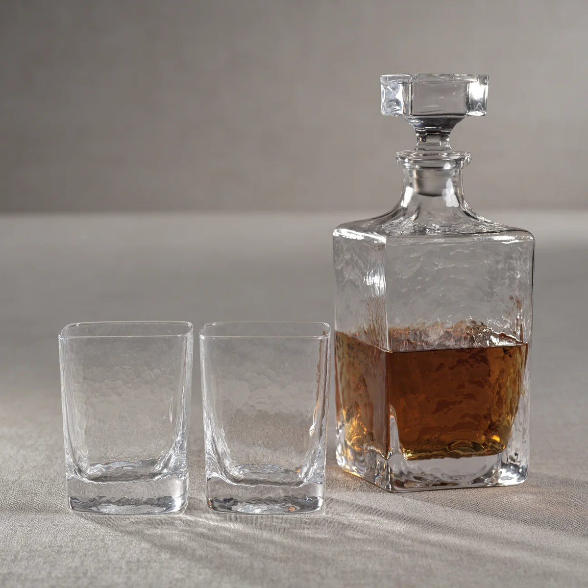 The ZODAX PUNTA MITA Hammered Glass Decanter is a clear, rectangular 32 oz vessel with a square faceted stopper and textured glossy finish, shown against a plain white background.