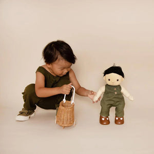 A DINKUM DOLL from OLLI ELLA USA features soft brown hair and comes dressed in a white knit romper paired with brown shoes. This charming doll has an embroidered face with brown eyes, a small nose, and a gentle smile. Its posable body makes it perfect for imaginative playtime, and it is posed standing upright.