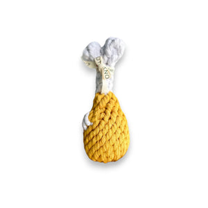 A hand holds the KNOTTY PAWS - CLUCKY DRUMSTICK DOG TOY by KNOTTY PAWZ, resembling a drumstick with yellow yarn as the fried top and white/brown fabric as the bone. Perfect for pups!.