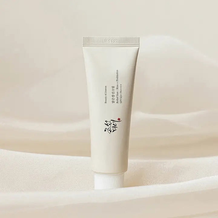 A white, cylindrical tube of BEAUTY OF JOSEON RELIEF SUN RICE AND PROBIOTICS from KOSMIC KBEAUTY SKINCARE stands upright against a plain background. The tube features East Asian characters and English text indicating product details, with a white screw cap attached at the bottom.