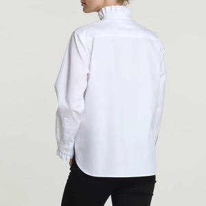 A person wearing the HINSON WU - NORA SHIRT, a luxe cotton blouse with delicate ruffles adorning the collar and cuffs, paired with black pants. This tailored shirt by HINSON WU features a button-up front with exquisite ruffle trim against a plain light background.