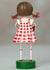 The ESC AND COMPANY - SWEET CAROLINA FIGURINE by ESC AND COMPANY, INC is a charming 6" poly resin figure. It features a girl with brown pigtails in a red-and-white checkered dress, standing on a green base, with her back turned and white socks accented by red stripes.