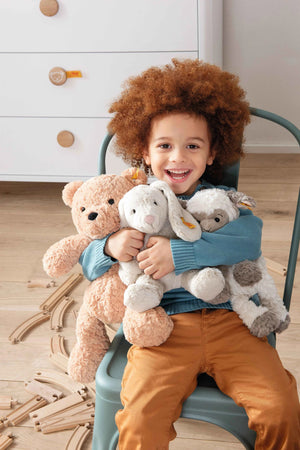 The STEIFF - JIMMY TEDDY BEAR, from STEIFF, is a fluffy beige stuffed bear with a friendly expression. It features a small, round black nose and eyes. Made from plush fabric, it has an ear tag and sits upright against a plain white background.