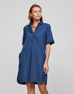 A woman with long dark hair, facing away, wears the HINSON WU - AILEEN Short Sleeve Denim Dress in light blue tencel, featuring a button-down back. She stands against a plain gray background.