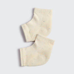 A pair of MOISTURIZING HEEL SOCKS by KITSCH in an off-white color with small, colorful speckles are laid out side by side on a gray background. These socks feature a ribbed cuff and are designed to fit over the ankle, ensuring a smooth feel for delicate skin.