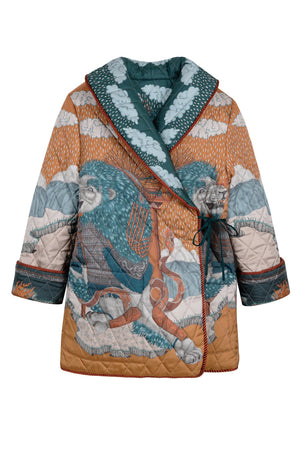 A person wears the SABINA SAVAGE - THE SNOW LION QUILTED JACKET from SABINA SAVAGE ENGLAND, featuring a colorful, intricately designed nature-themed pattern with trees, sky, and animals. Reminiscent of a reversible silk twill jacket, it features a wide collar, contrasting orange inner lining, and large pockets. The person is shown from the shoulders down.