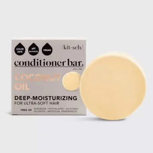 A round, beige solid moisturizer sits atop a white box labeled "KITSCH COCONUT REPAIR DEEP CONDITIONING BAR MASK." The box also indicates that the coconut oil conditioner is color safe, pH balanced, vegan, and weighs 2.7 oz (77g).