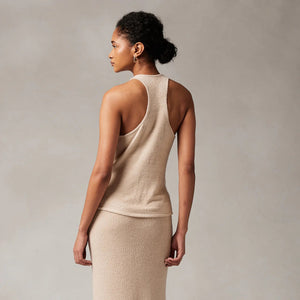 A woman with curly hair tied in a low bun is wearing the KASHWERE COWL NECK TOP by KASHWERE, paired with a matching knit skirt. She stands against a neutral background, facing to the left and showcasing the back of her outfit, which hints at athleisure vibes.