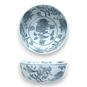 The HAND STAMPED PORCELAIN BOWL WITH BIRDS by CREATIVE COOP is a set of white stoneware bowls adorned with intricate blue botanical and bird designs. In the images, one bowl is presented in a top-down view, showcasing its detailed inner hand-stamped pattern, while the other is displayed from the side to emphasize its exterior design. Both bowls are photographed against a plain white background.