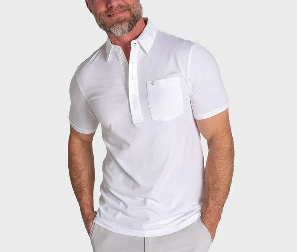 A bearded man wearing the CRIQUET Top Shelf Players Shirt in White, a classic fit short-sleeve Pima cotton shirt with a front pocket, stands against a plain light gray background.