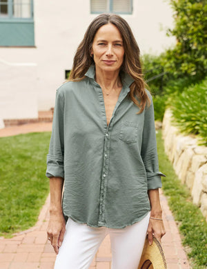 The FRANK & EILEEN - EILEEN RELAXED BUTTON UP SHIRT IN FAMOUS DENIM THYME is a light green, long-sleeved button-up shirt with a single chest pocket. The sleeves are rolled up to the elbows, and the fabric has a slightly crinkled texture. Featuring Eileen's relaxed fit, this shirt includes bust-flattering button placement, a high-low hem, and a collar without a visible tag.