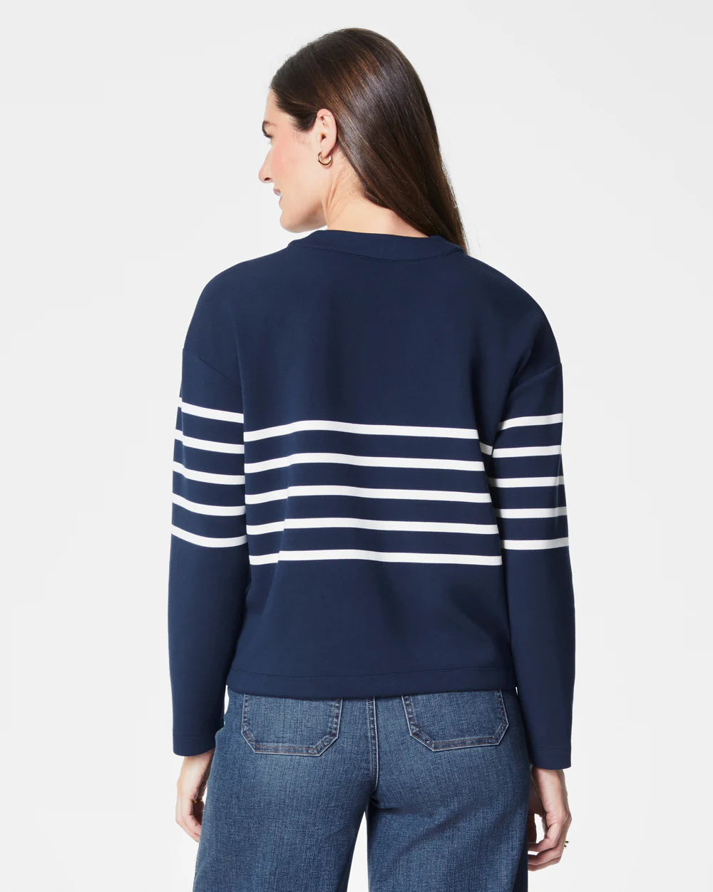 A person with long dark hair smiles confidently while wearing the SPANX AireEssentials Stripe Cardigan in navy blue, crafted from super-soft fabric featuring white horizontal stripes, paired with dark blue jeans, against a plain white background.