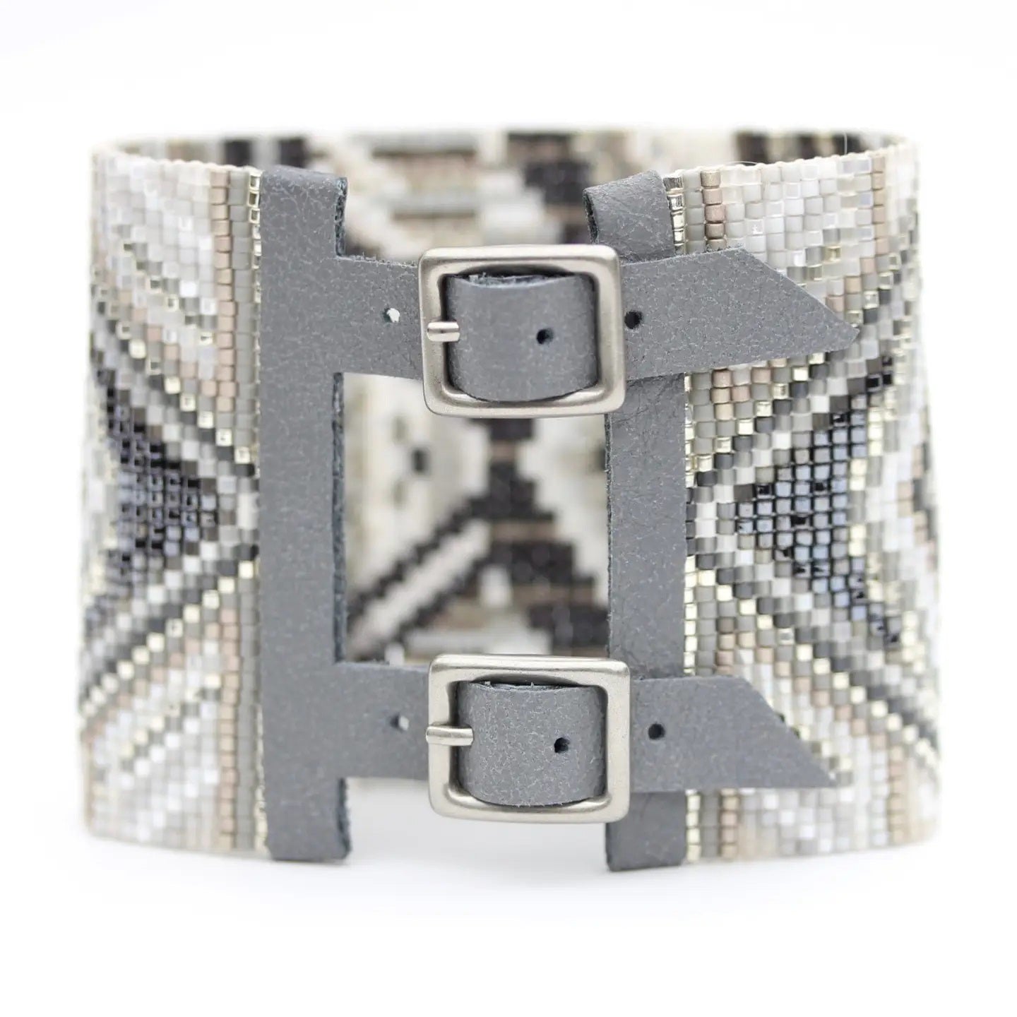 The JULIE ROFMAN - HORIZON CUFF from JULIE ROFMAN JEWELRY is a handwoven glass beaded delica bracelet that showcases an intricate geometric pattern in black, white, and gray. The design includes diamond shapes and symmetrical lines for a mosaic-like appearance, finished with an adjustable buckle clasp to ensure a perfect fit.