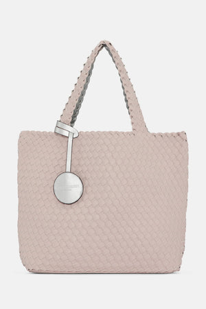 The WOVEN REVERSIBLE TOTE BAG by LINES OF DENMARK is a white tote featuring two shoulder straps and a circular faux-leather tag on one strap. This shopper showcases a textured, interlaced pattern and reversible design, providing stylish and elegant dual styling options. The image background is plain white.