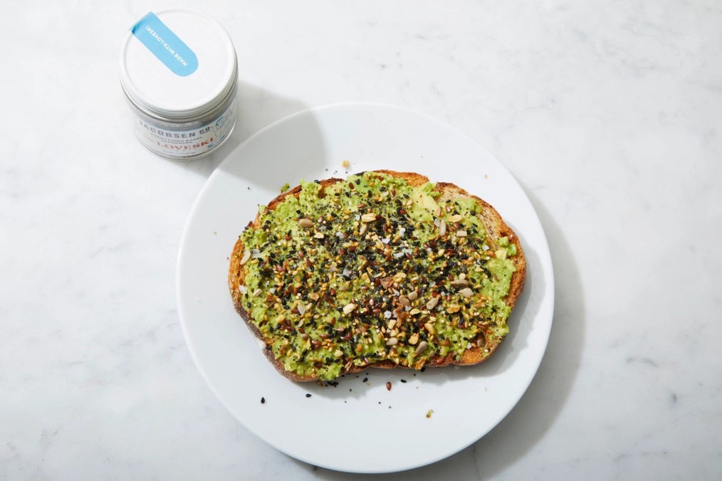 A small glass jar of Jacobsen Salt Co. Everything Bagel Seasoning, a collaboration with Loveski, sits on a flat surface against a plain light gray background. The jar's label is white with blue and red text and features cartoon illustrations. Perfect for your homemade sourdough bagels, this blend of seasonings stems from Northern California's artisanal traditions.