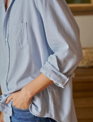 The Eileen Relaxed Button Up Shirt in Gray Blue by Frank & Eileen features a chest pocket, rolled-up sleeves, and bust-flattering button placement. Its inside label says "Frank & Eileen EST. 1947," and it is shown laid flat against a white background.