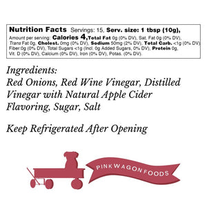 A clear jar with a white lid, labeled "PINK WAGON- PICKLED PINK ONIONS." The jar contains sliced Pacific Northwest onions in a pickling solution, filling the entire container. The label, branded with "PINK WAGON FOODS," features decorative red and white elements and indicates a net weight of 12 fl oz (355 ml).