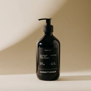 A dark bottle of PRESTON - CONDITIONER with a pump top, labeled "Preston Softening and Shine Conditioner." The label also includes text stating "Made in USA," "16 oz / 500 ml," and "cruelty free." Infused with Indian Amla Oil, this nourishing conditioner is set against a neutral background with a shadow cast on the right.