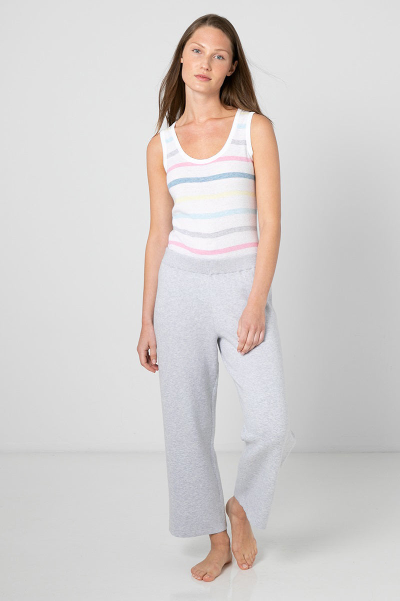 A woman with straight brown hair is standing barefoot in a relaxed pose. She is wearing a white sleeveless top made of soft cotton with pastel-colored horizontal stripes, paired with light gray KINROSS CASHMERE - DOUBLE KNIT CROP PANT by KINROSS. The background is plain and white.