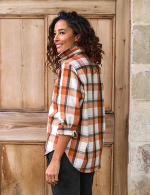 The FRANK & EILEEN Eileen Relaxed Button Up Shirt in Italian Flannel Pumpkin Plaid is a long-sleeved, button-up design featuring a flattering button placement at the bust and a classic collar. It showcases an orange, white, and brown plaid pattern with stylishly rolled-up sleeves. Additionally, the brand label is visible on the inside of the collar.