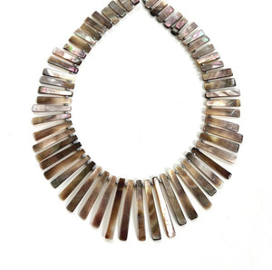 The ANN LIGHTFOOT - REVERSIBLE SHELL RAS DU COU FAN NECKLACE by ANN LIGHTFOOT features multiple rectangular shell pieces, arranged in a graduated design. These shells display iridescent shades of brown, gray, and hints of pink, creating a harmonious and elegant look.