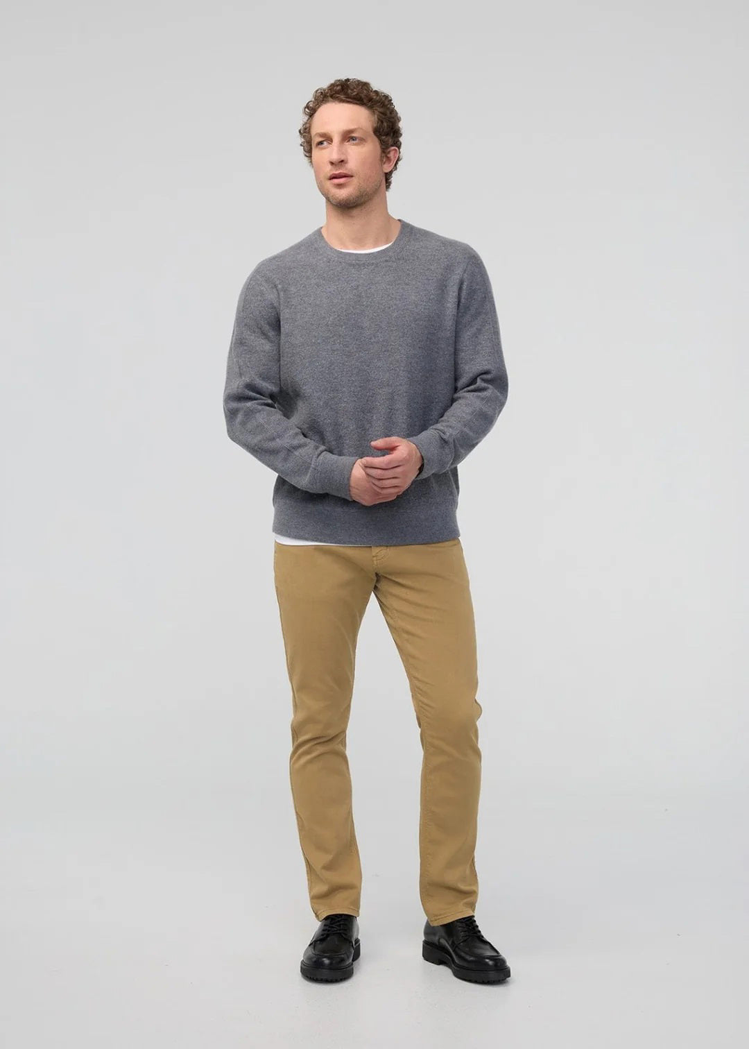 A man with short dark hair and a trimmed beard stands against a white background, wearing a white t-shirt, white sneakers with black details, and DUER&#39;s DU/ER NO SWEAT RELAXED TAPER PANT in an athletic fit. One hand is in his pocket.