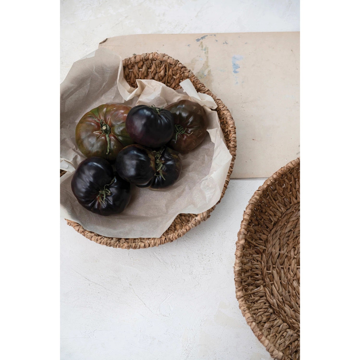 Displayed against a plain white background are two circular woven wicker baskets of different sizes. Reminiscent of the BRAIDED BANKUAN BOWL WITH SCALLOPED EDGE (LARGE) by CREATIVE COOP, these baskets feature a natural, rustic appearance with a textured finish and slightly irregular edges.