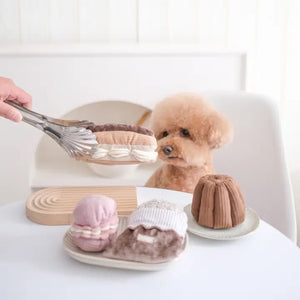 A plush toy named the "LAMBWOLF COLLECTIVE - ECLAIR DOG TOY" by LAMBWOLF COLLECTIVE sits on a white background. The toy features multiple textures with light brown "pastry" sides, a dark brown "chocolate" top, and white "cream" filling, mimicking the appearance of a real snuffle eclair dessert.