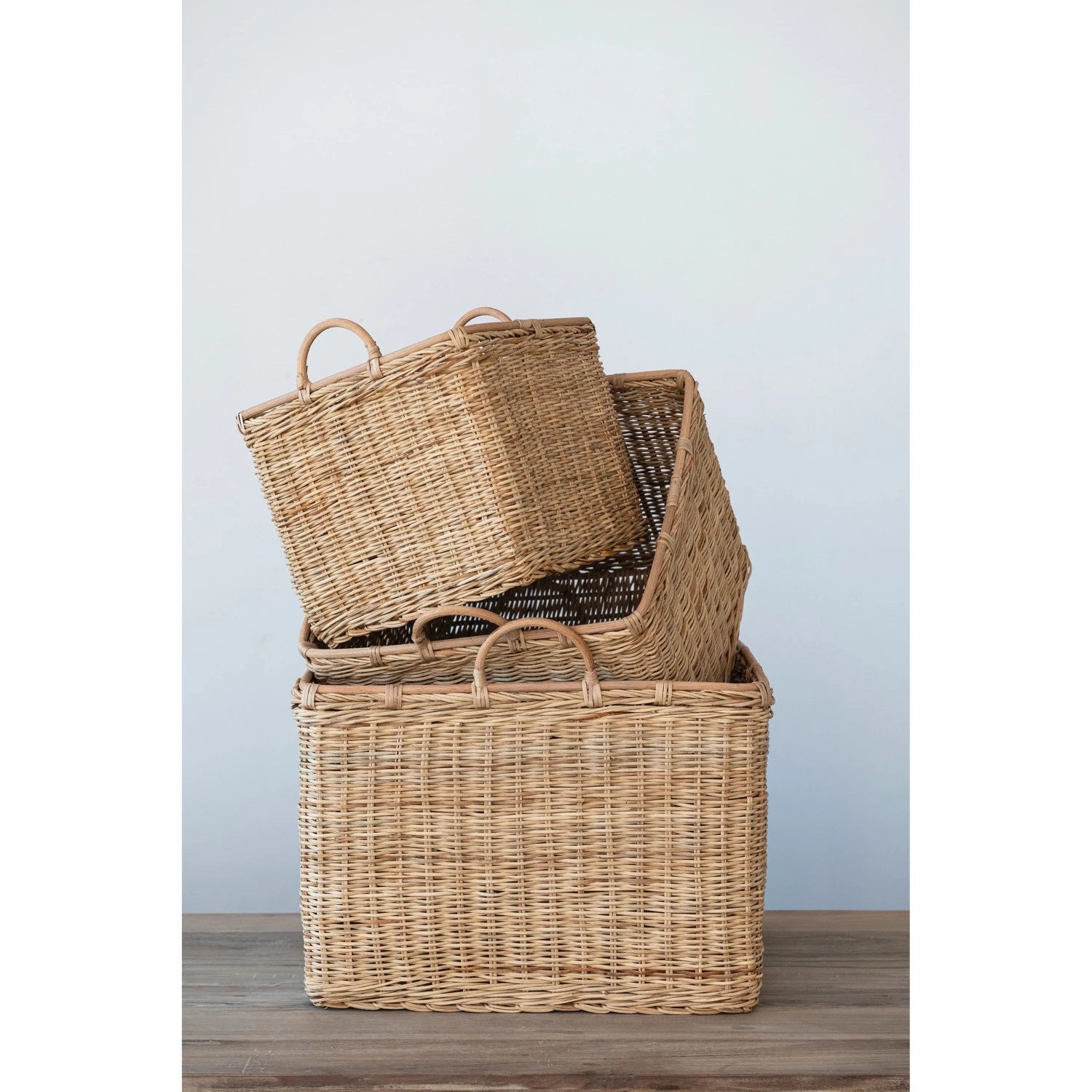 Three RATTAN BASKET WITH HANDLES (MEDIUM) by CREATIVE COOP of varying sizes are shown side by side. The light brown baskets, featuring two small handles on top for easy carrying, offer an eco-friendly storage solution. Each basket is slightly larger than the one next to it, perfect for bohemian decor.