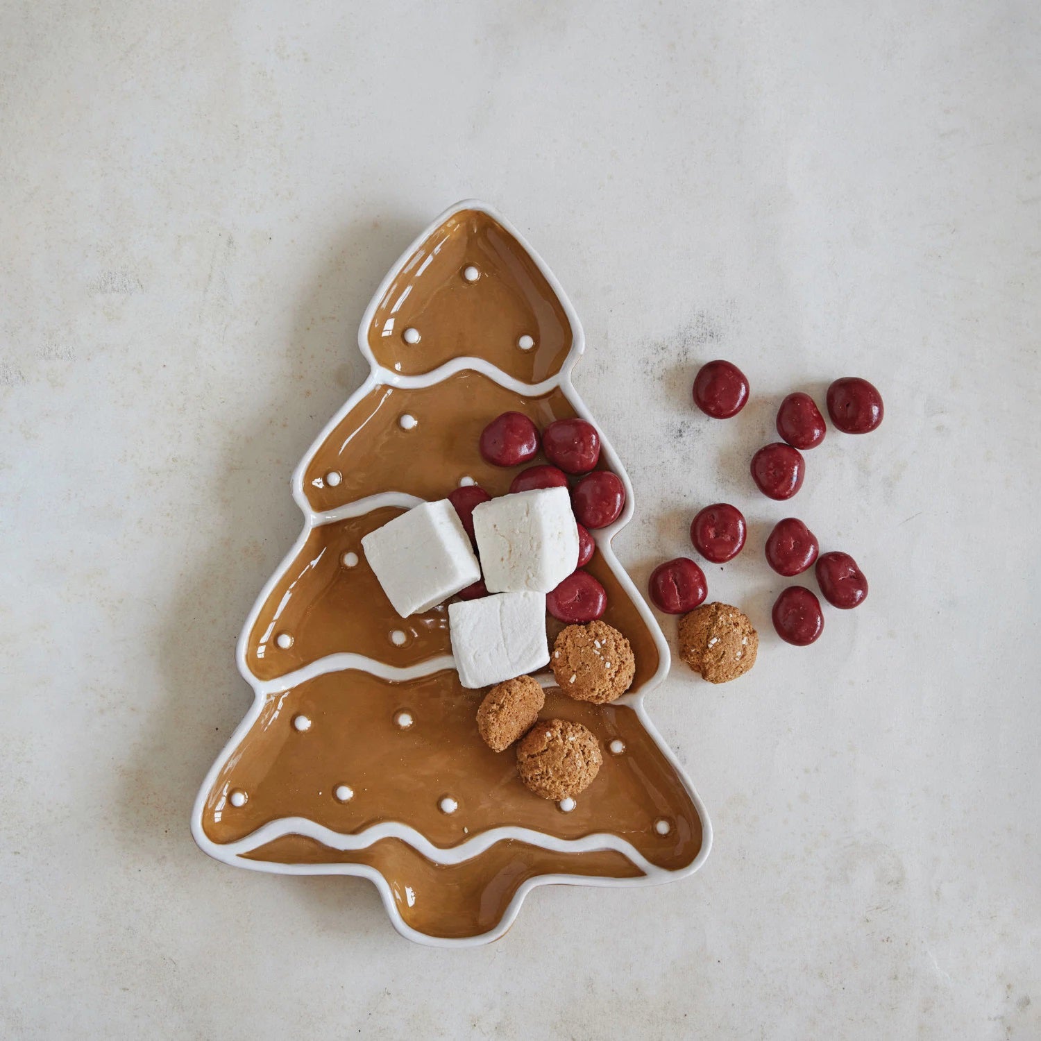 The GINGERBREAD TREE PLATTER by CREATIVE COOP, designed with a charming gingerbread tree motif, is perfect for holding marshmallows, small cookies, and red candies. Styled on a light surface, it brings a festive and cozy holiday atmosphere to your setting.