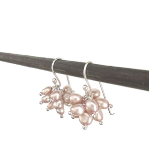 The ANN LIGHTFOOT Pale Pink Freshwater Pearl Cluster Earrings elegantly hang on a dark rod, featuring clusters of small pearls with a smooth, shiny surface in a floral design attached to sterling silver earwires, adding sophistication.