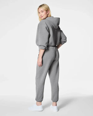 A person in SPANX - AirEssentials Jogger Pant in Heather Gray with a drawcord waist and matching sweatshirt stands with hands in pockets, paired with white sneakers. The luxuriously soft fabric against a plain white background highlights their cozy, relaxed style.