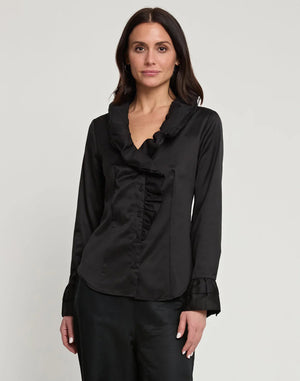 A woman with long dark hair is wearing the HINSON WU - AMARA LONG SLEEVE COTTON SATIN SHIRT in black, featuring ruffled details along the collar and front buttons. She stands facing the camera against a plain, light-colored background.