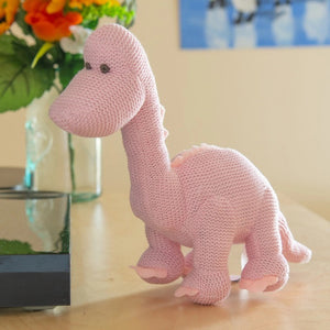 The DARK PINK KNITTED DIPLODOCUS TOY from BEST YEARS LTD stands against a white background. This soft, plush dinosaur features a long neck, small brown eyes, and short, stubby spikes along its back and tail. Its cozy texture makes it perfect for hugging—a delightful addition to newborn gifts.